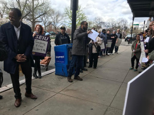 GETTING AN EARFUL: Emerson President Lee Pelton, left, and staff member Anna Feder, with sign, listen as staffer Pierre Huberson talks to a luncheon rally for equal pay and a fair wage.