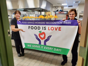 FOOD SERVICE WORKERS HONORED: Pegge Minkle, left, chapter president, and June Iadorola held a “Food Is Love” banner last fall. Both of them served on the negotiating team for the Local 888 cafeteria chapter in Hopkinton.